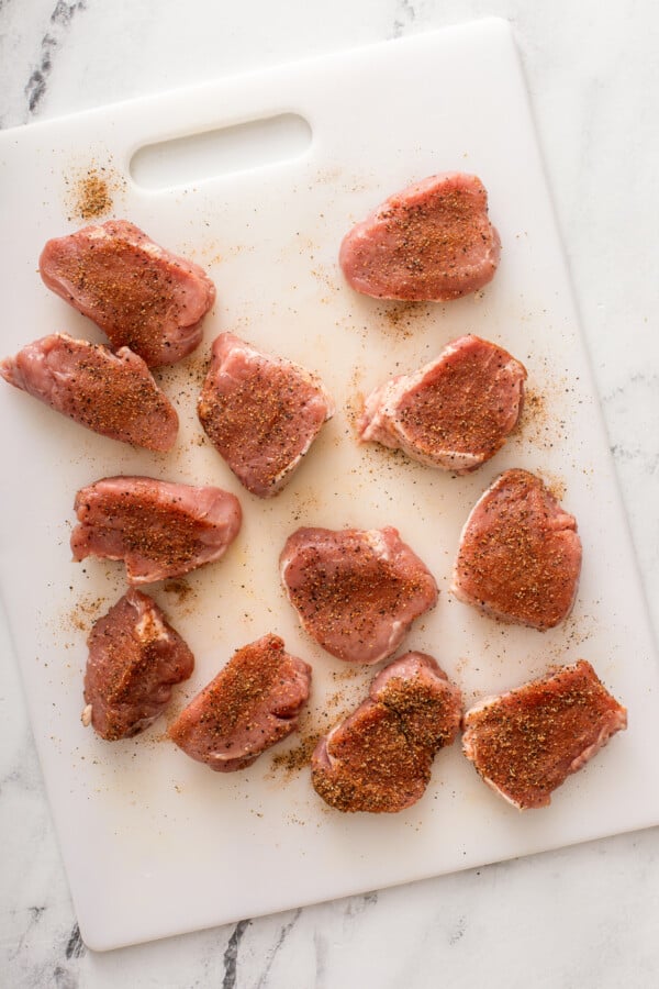 Pork tenderloin is being seasoned on a cutting board. 