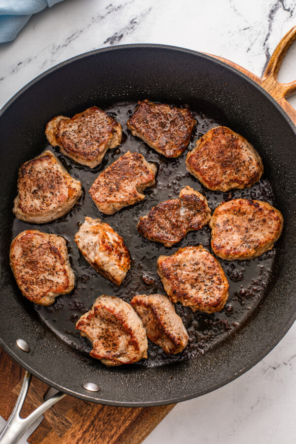 Pork is being seared in a skillet. 