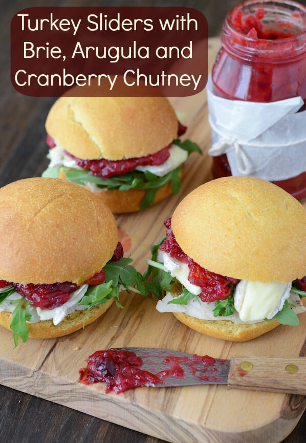 Three Turkey Sliders loaded with brie, arugula and cranberry chutney on a wood board