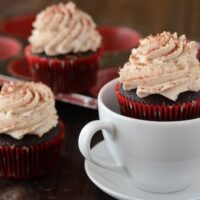 A Spicy Hot Cocoa Cupcake in a White Mug Beside Two More Frosted Cupcakes