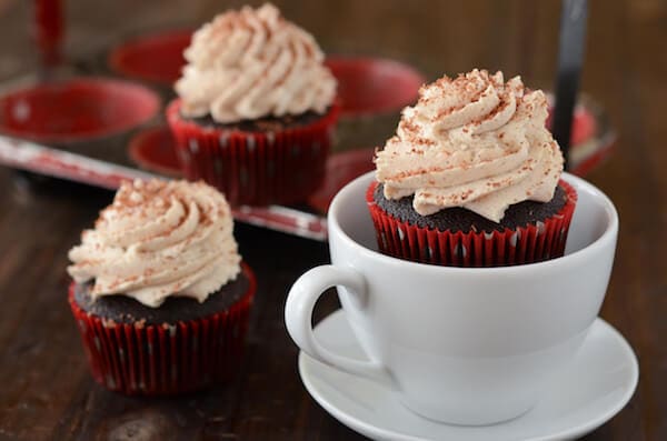 A Spicy Hot Cocoa Cupcake in a White Mug Beside Two More Frosted Cupcakes