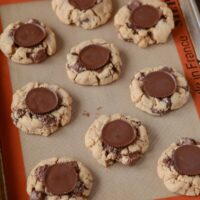 Peanut Butter Cookies topped with Reese's Cups sit on a baking sheet