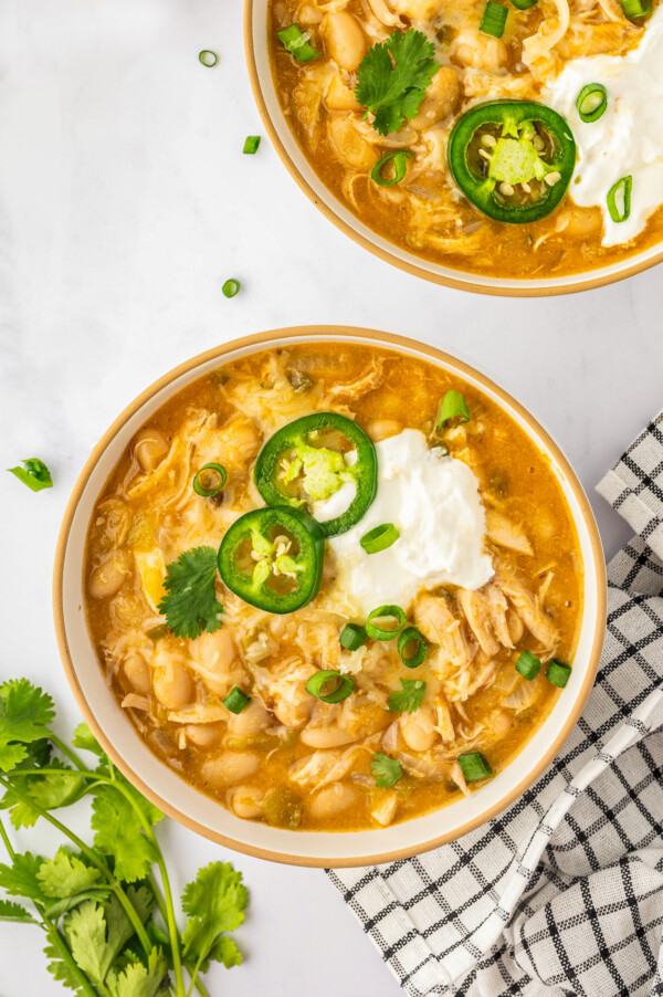 Overhead view of a bowl of white bean chicken chili with jalapeño slices and sour cream on top.