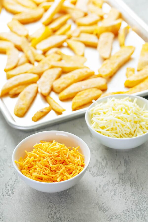 Fries on a sheet pan and two types of cheese to make cheese fries.