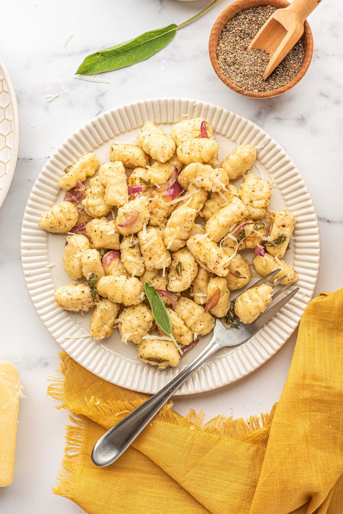 Overhead shot of a serving of gnocchi in brown butter sauce, on a white plate with a fork.