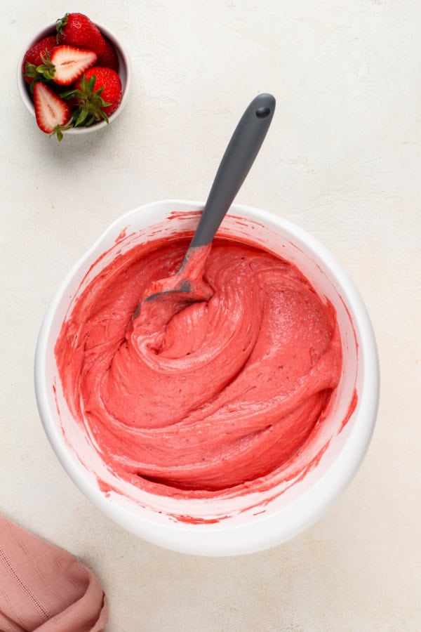 Pink cake batter is being mixed in a large white bowl.