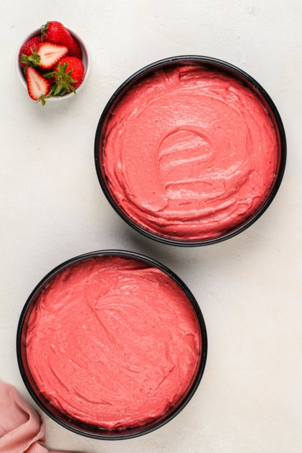 Strawberry cake batter is spread evenly between two cake pans.