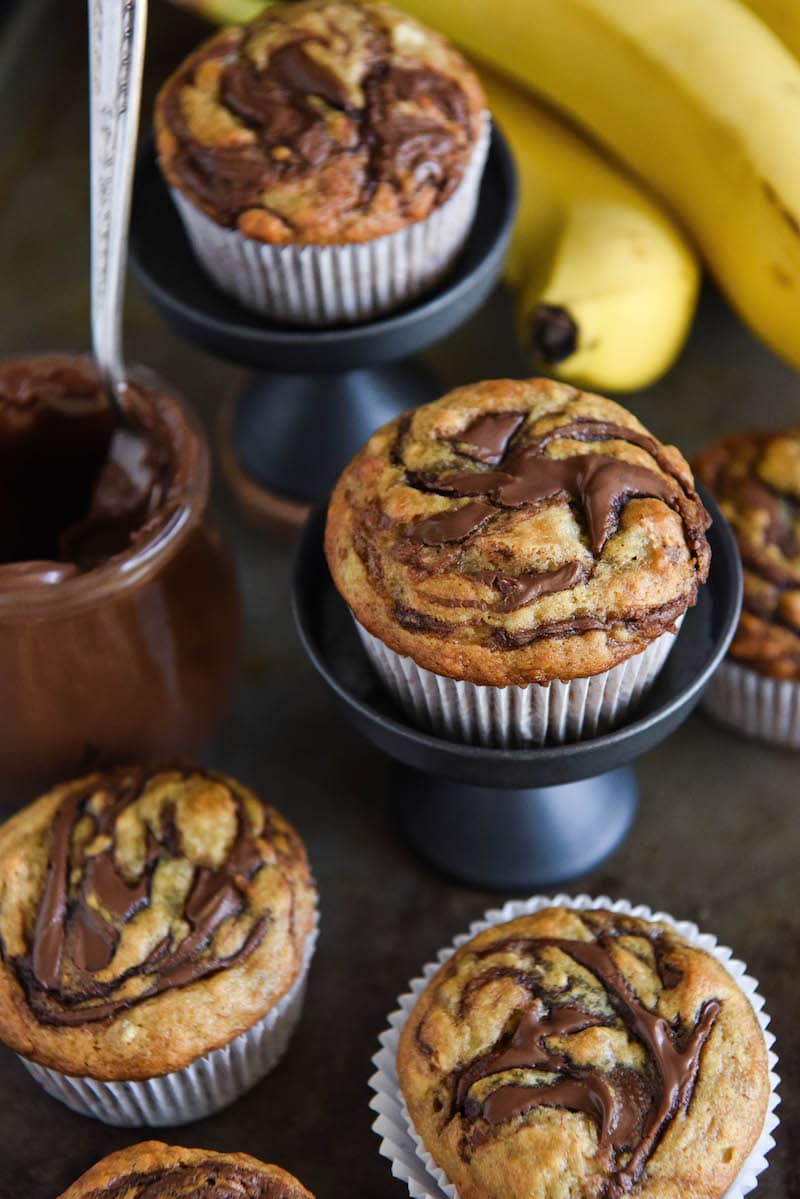 Nutella topped muffins in muffin wrappers on a cookie sheet with a jar of Nutella. 