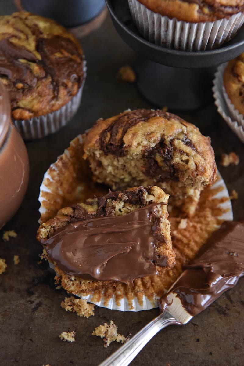 A banana nutella muffin sliced in half with a small knife spreading more Nutella on the muffin. 