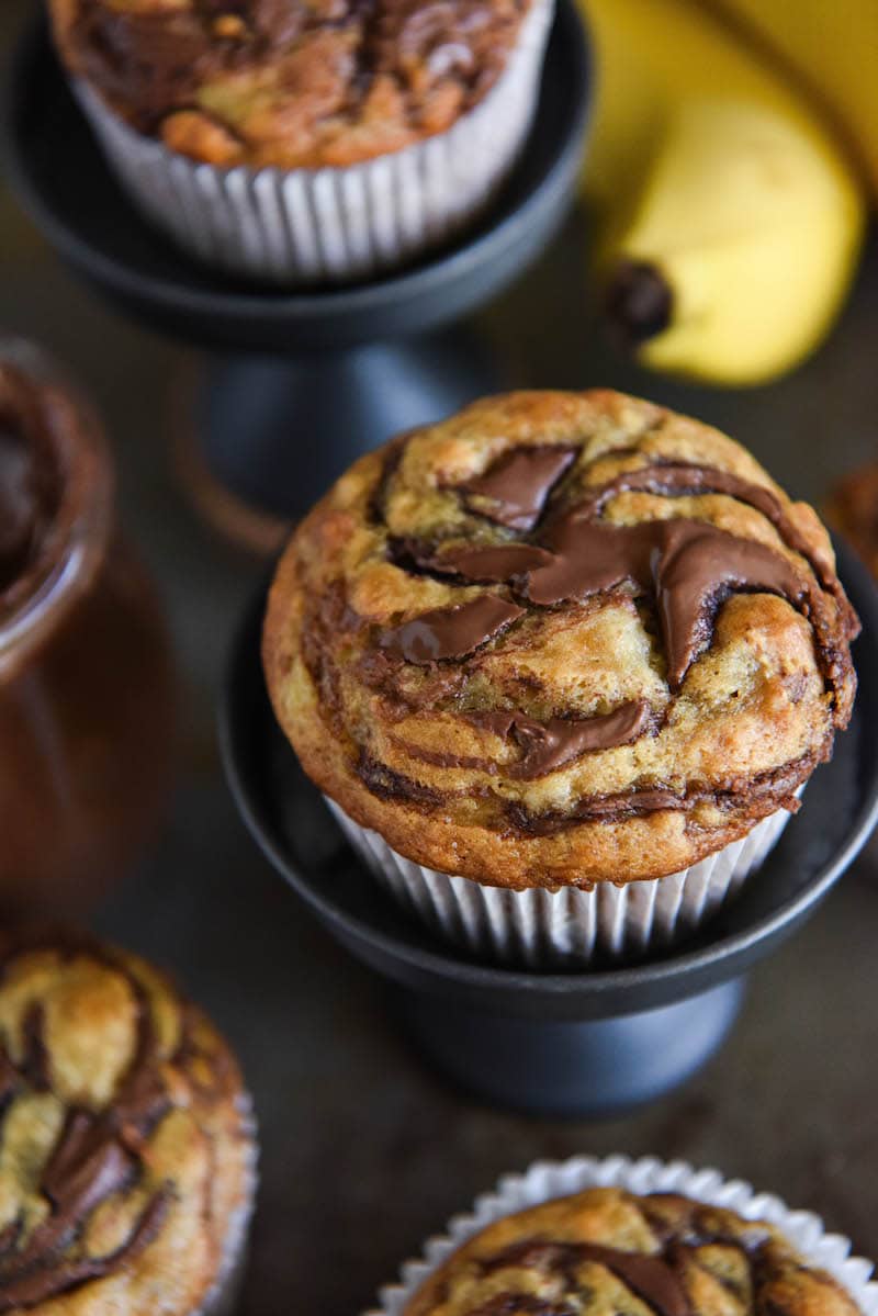 Two Nutella Banana Swirl Muffins on cupcake trays with bananas in the background. 