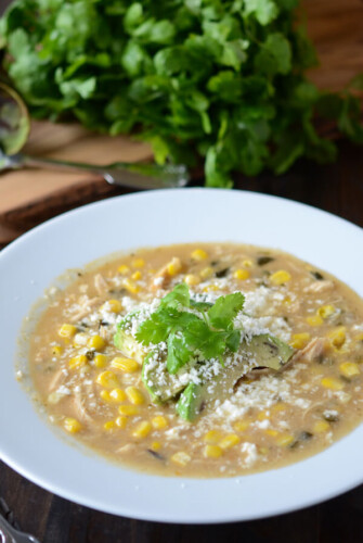 Creamy Corn and Chicken Soup with Roasted Poblano in white bowl, garnished with avocado slices.
