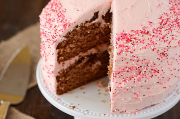 Strawberry frosted cake with slice cut out on a white plate