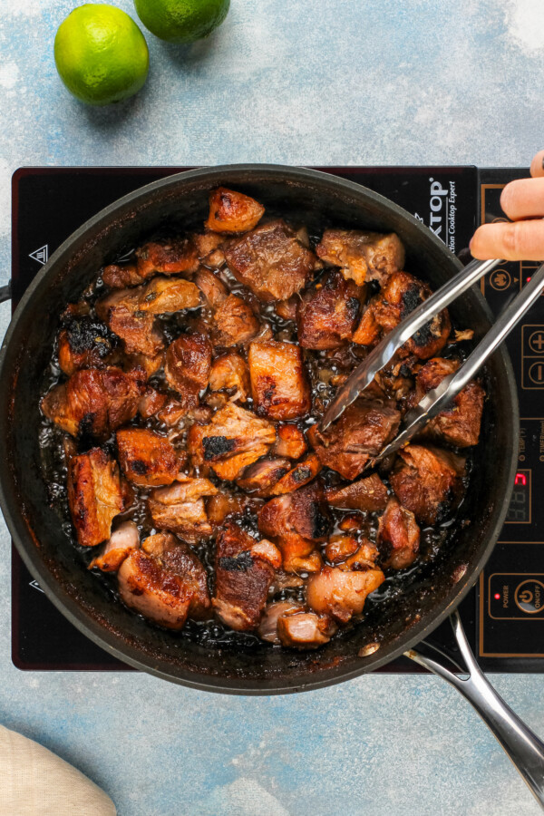 Browning the carnitas in the pot until crispy.