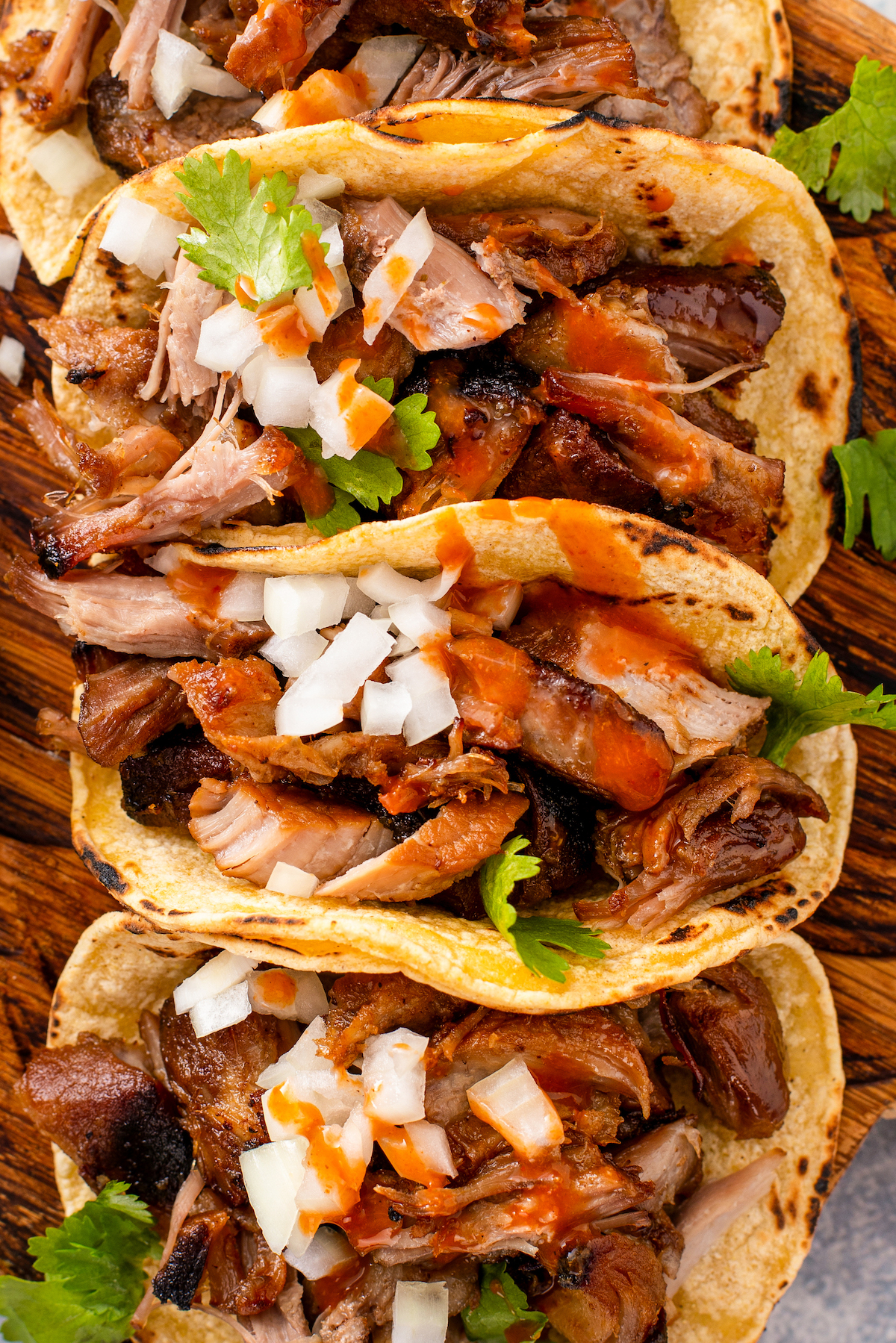 Close-up of three pork carnitas tacos with cilantro, hot sauce, and diced onions. 