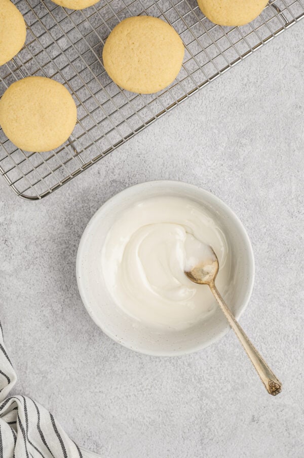 A wire rack of cookies next to a bowl of almond glaze.