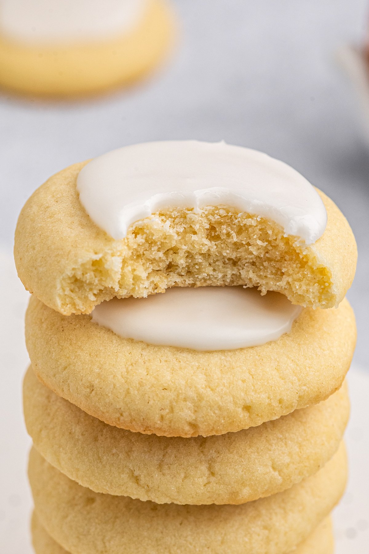 A stack of soft sugar cookies with almond glaze. The top cookie of the stack has had a bite taken out of it.