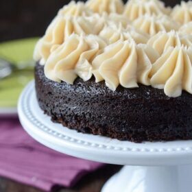 A Dark Chocolate Guinness Cake with Dollops of Bailey's Frosting on a White Cake Platter