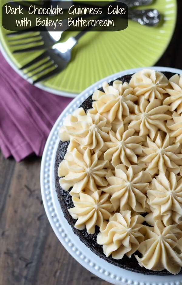 A Guinness Cake with Baileys Buttercream on a Cake Stand Next to a Plate with Three Forks