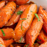 Close-up shot of candied carrots in a white bowl.