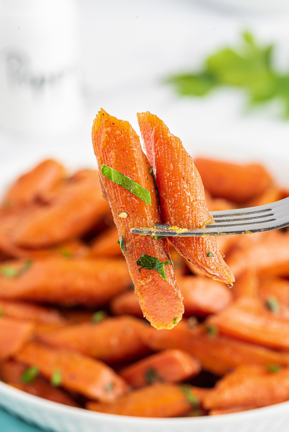 Two pieces of candy carrots on a fork, with a bowl of carrots in the background.