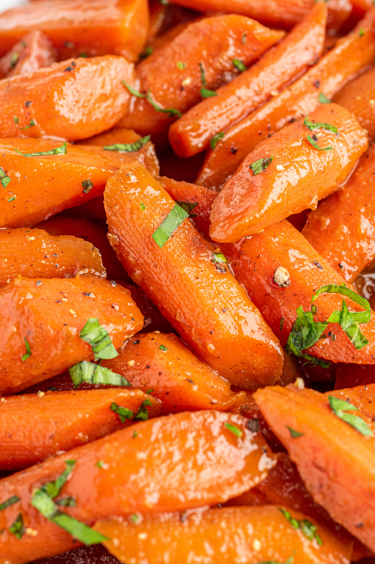 Close-up shot of candied carrots garnished with chopped herbs.