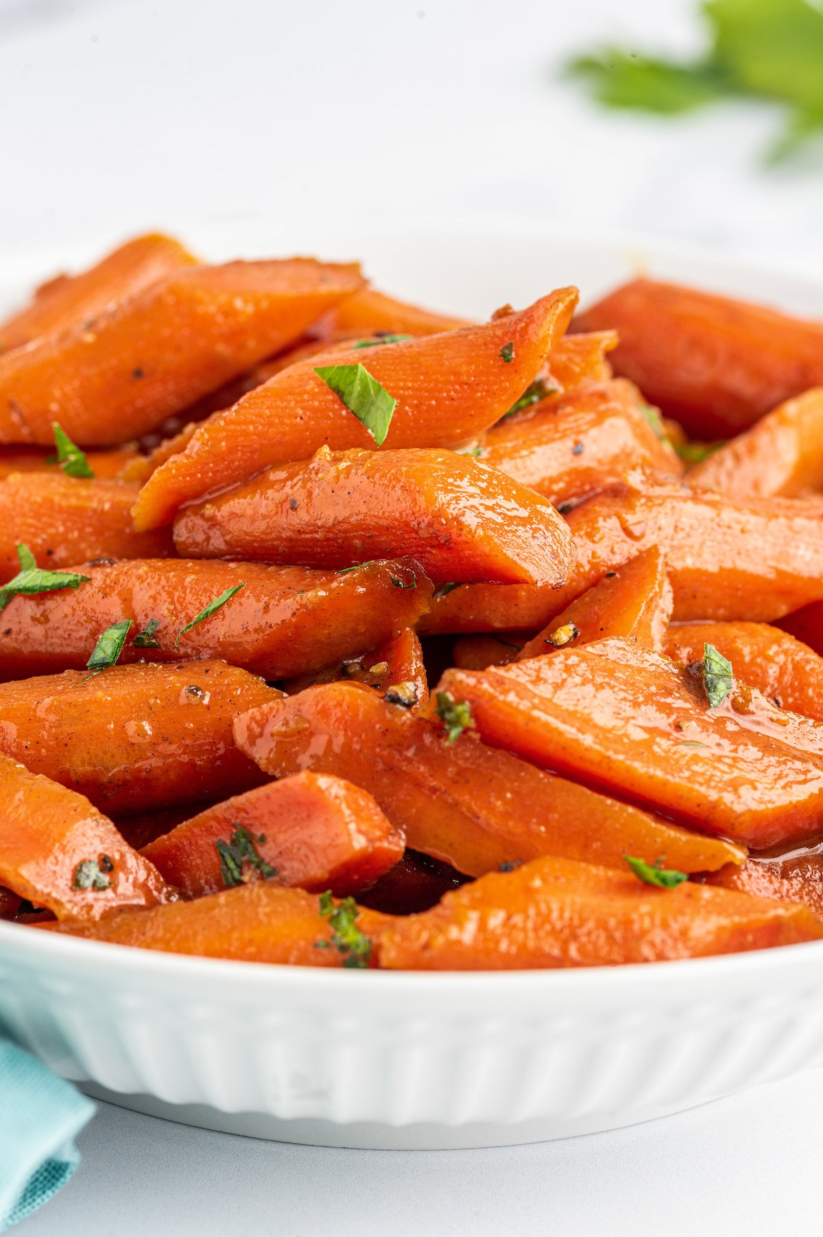 Side view of candied carrots piled into a shallow white dish.