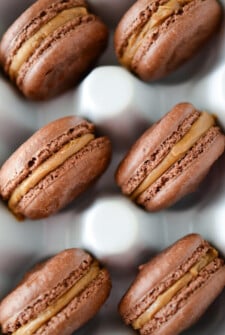 Chocolate Biscoff Macarons in a white ceramic egg container.