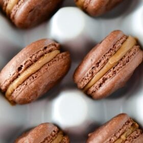 Chocolate Biscoff Macarons in a white ceramic egg container.