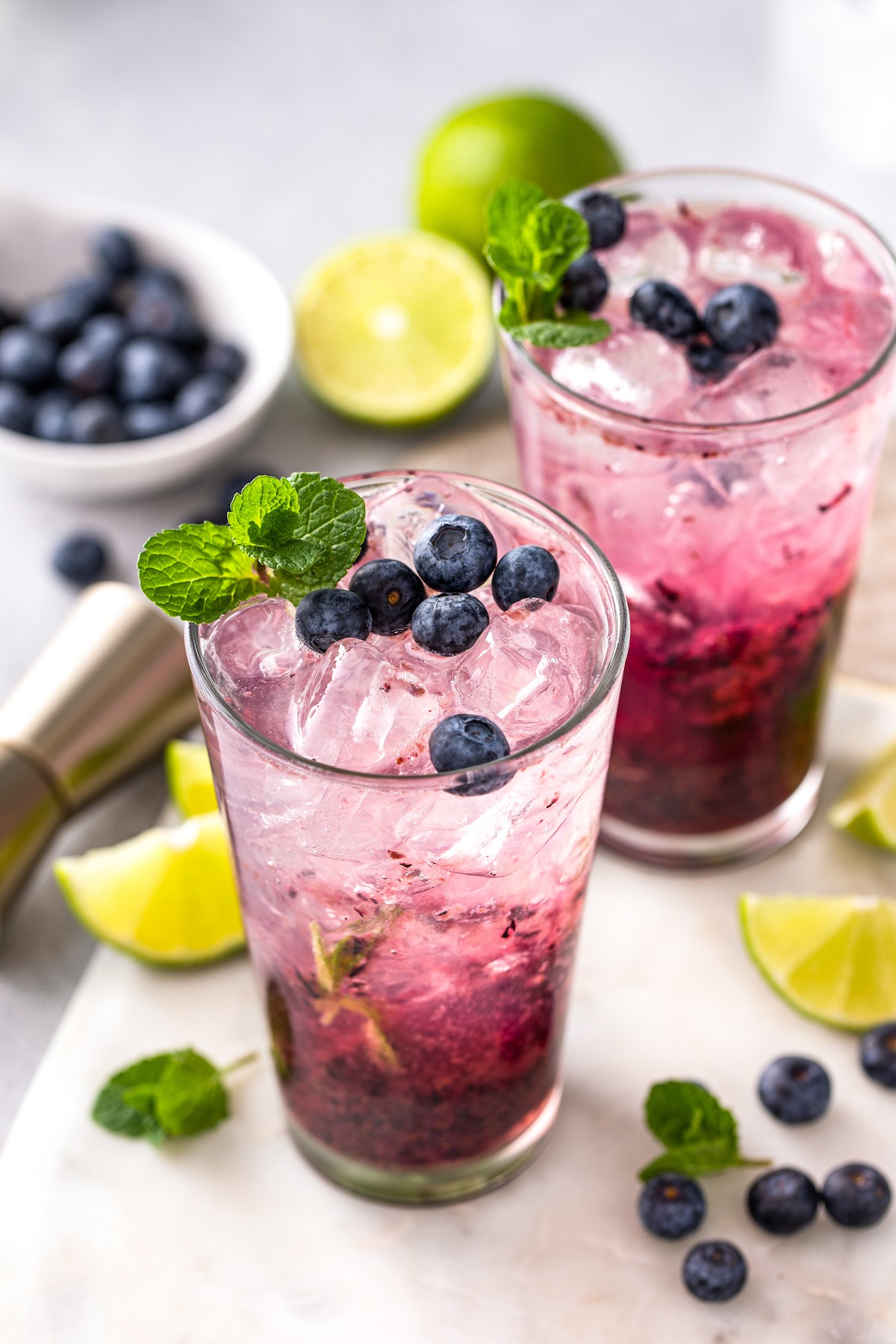 Two blueberry mojitos with mint and blueberries on top. 