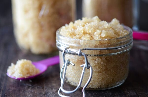 A Small Jar Full of Body Scrub Beside a Purple Spoon with a Scoop of Scrub