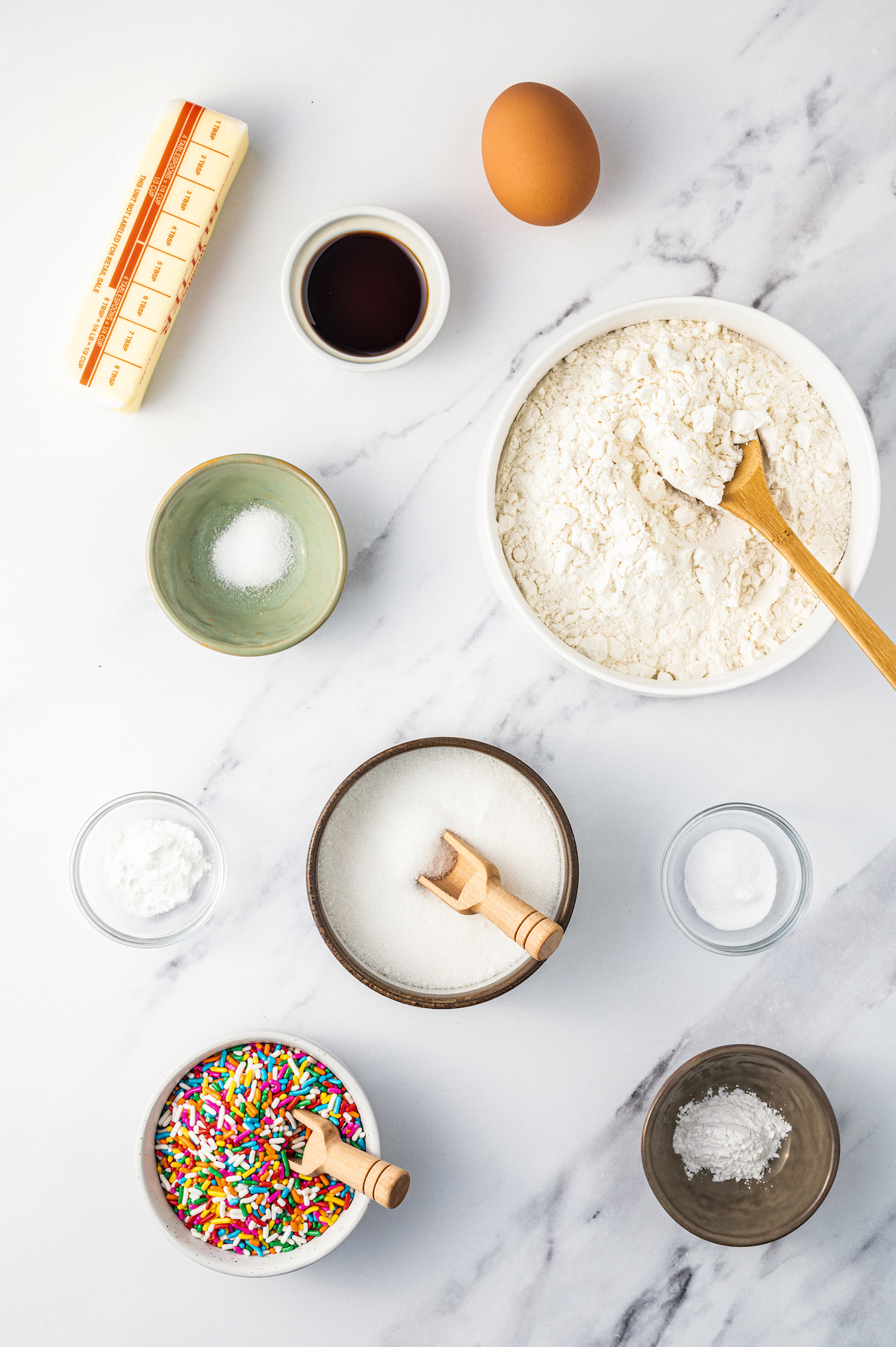 Sugar cookie ingredients and sprinkles on a work surface.