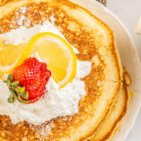Overhead shot of lemon ricotta pancakes. A sliced strawberry and lemon wedges are arranged on top.