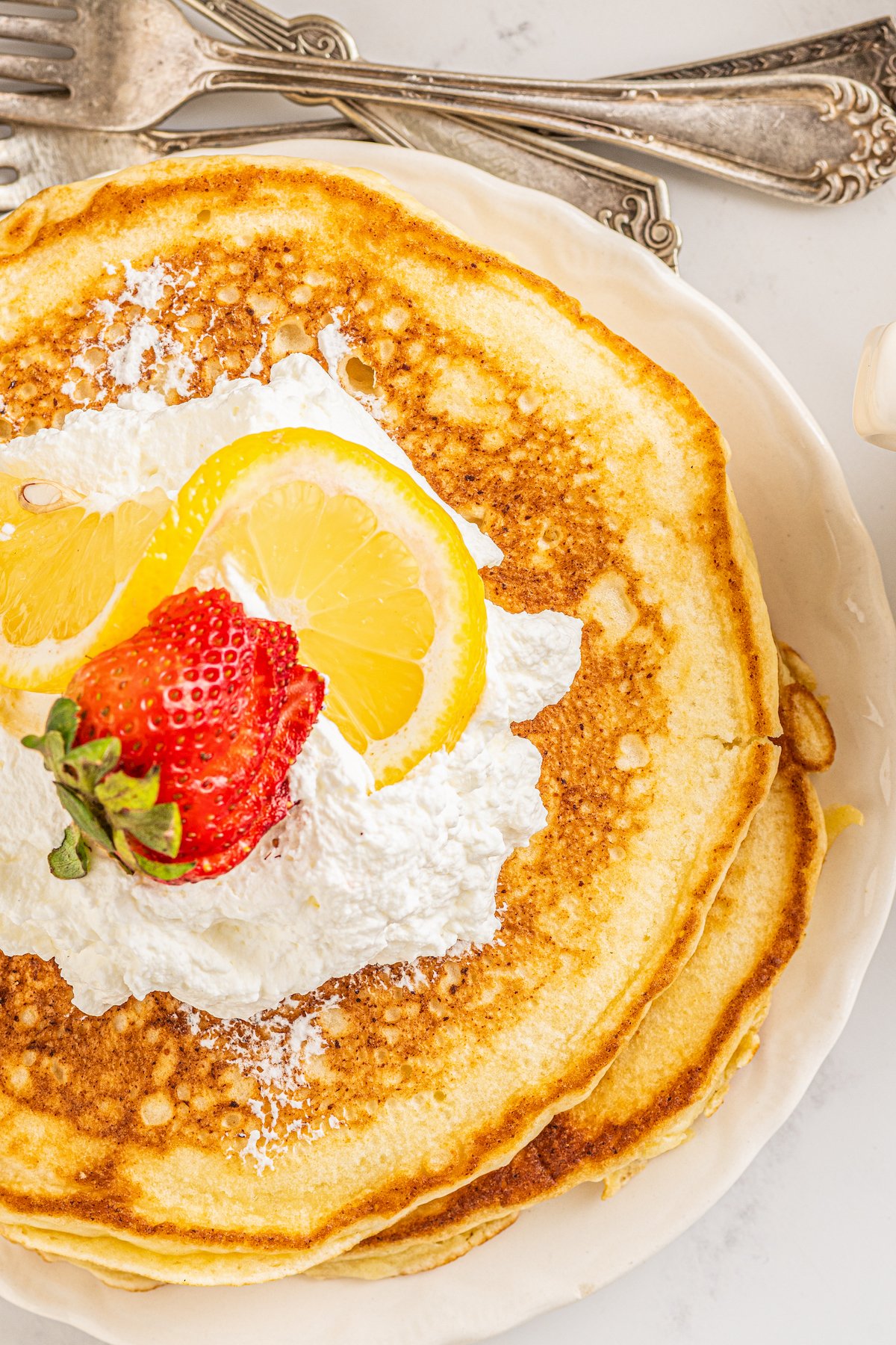 Overhead shot of lemon ricotta pancakes. A sliced strawberry and lemon wedges are arranged on top.