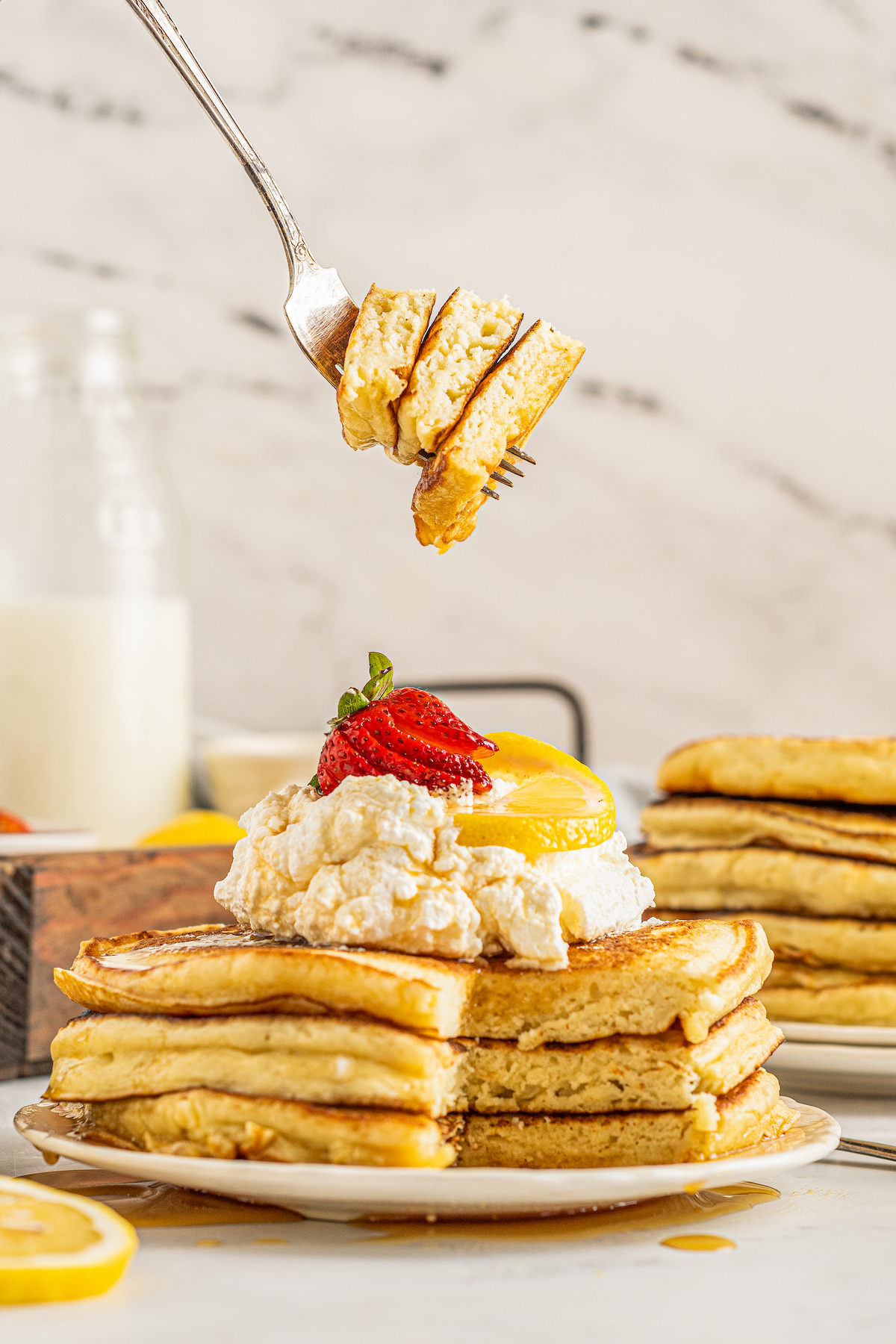 Pancakes on a plate. A bite has been cut from the pancakes and is being lifted away on a fork.