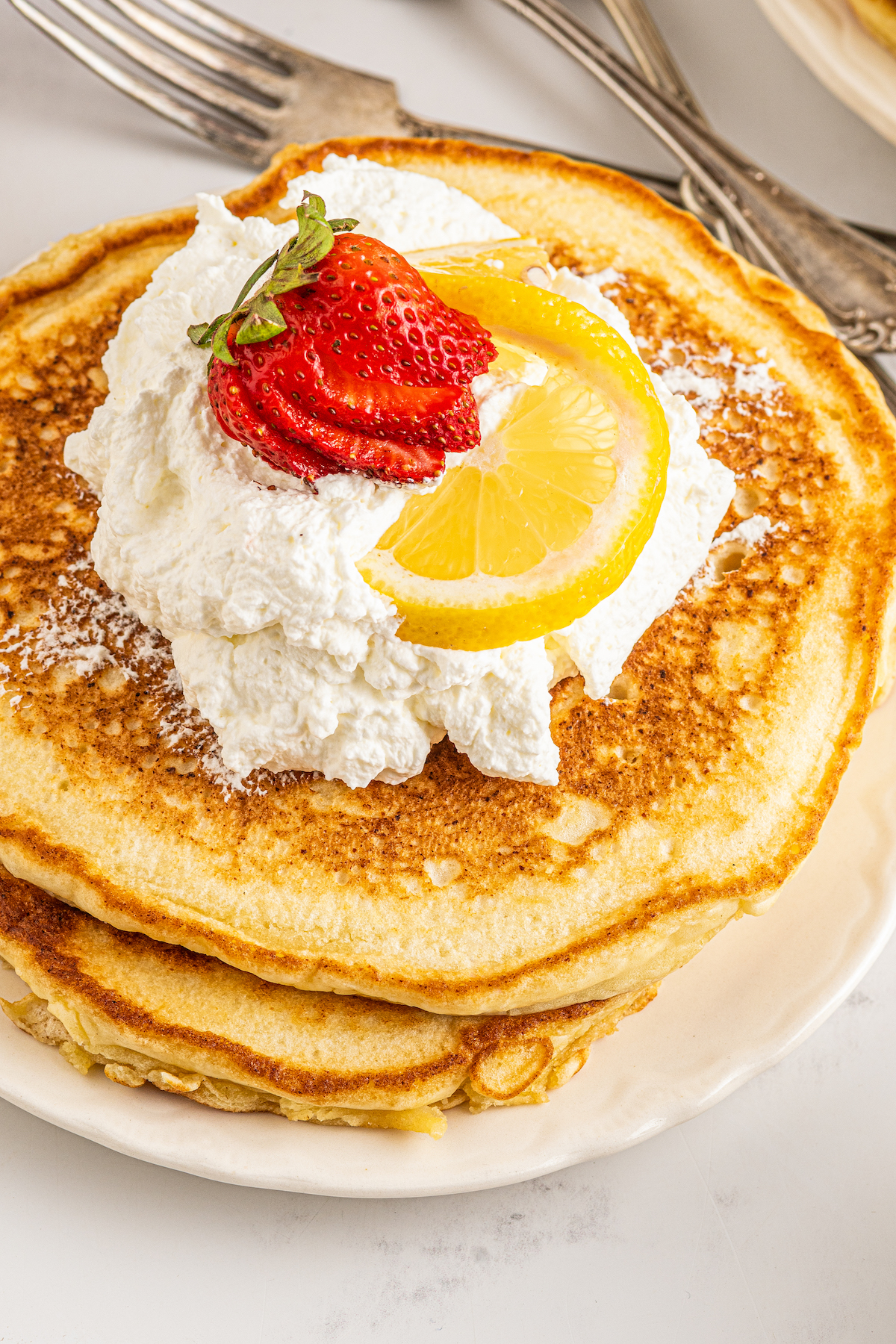 A stack of pancakes topped with whipped cream, berries, and lemon.