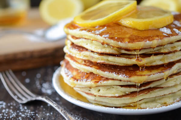 A stack of lemon ricotta pancakes topped with lemon slices and a drizzle of maple syrup.