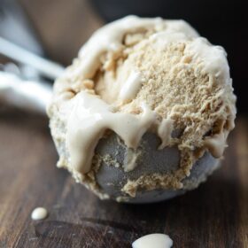 A scoop of Salted Caramel Ice Cream still in the ice cream scoop on a dark wooden board.