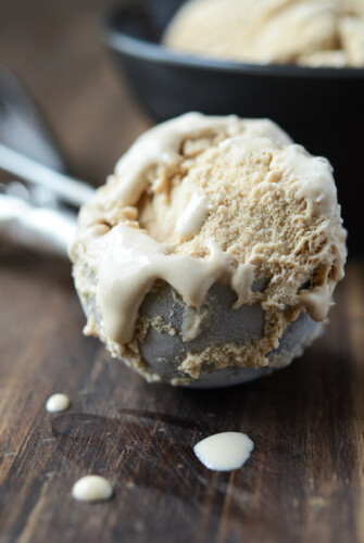 A scoop of Salted Caramel Ice Cream still in the ice cream scoop on a dark wooden board.