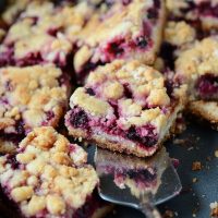 Blackberry Pie Bars topped with crumbles on a sheet pan with a serving utensil.