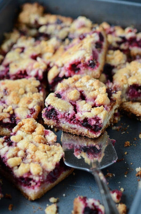 Blackberry Pie Bars topped with crumbles on a sheet pan with a serving utensil.