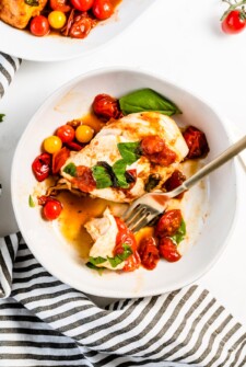 Plate of chicken with melted mozzarella and tomatoes.