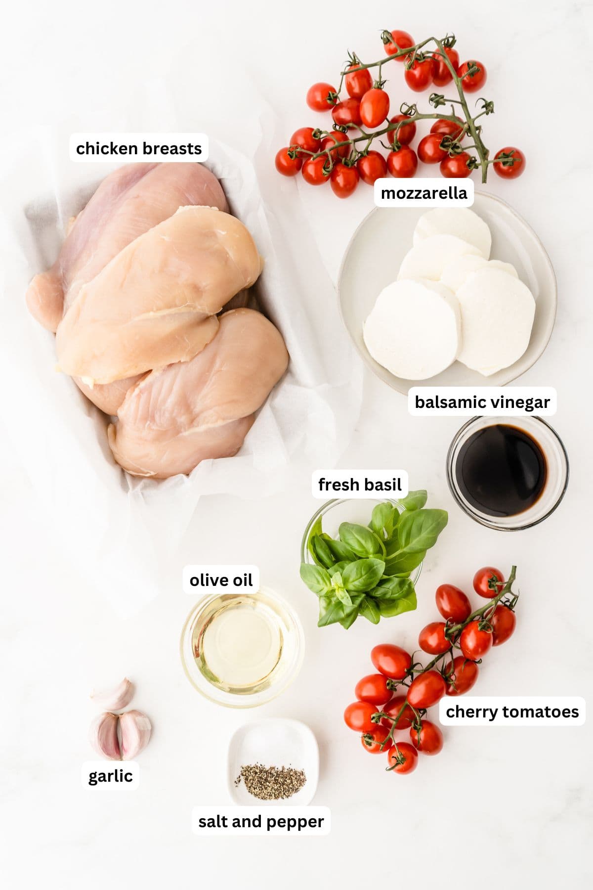 Ingredients for caprese chicken recipe in order from top to bottom: chicken breasts, mozzarella, balsamic vinegar, fresh basil, olive oil, garlic, salt and pepper, cherry tomatoes.