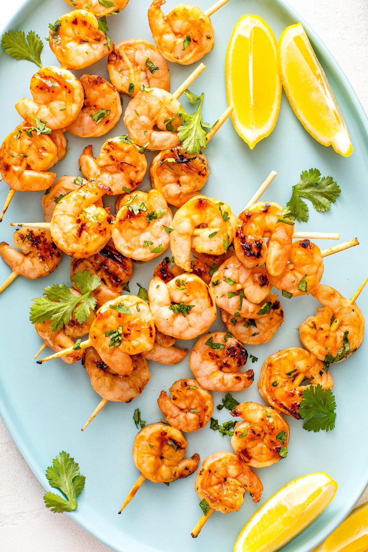 Grilled shrimp skewers on a plate with fresh cilantro and two lemon wedges.