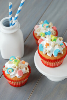 Three cupcakes in red wrappers topped with marshmallow frosting and lucky charms