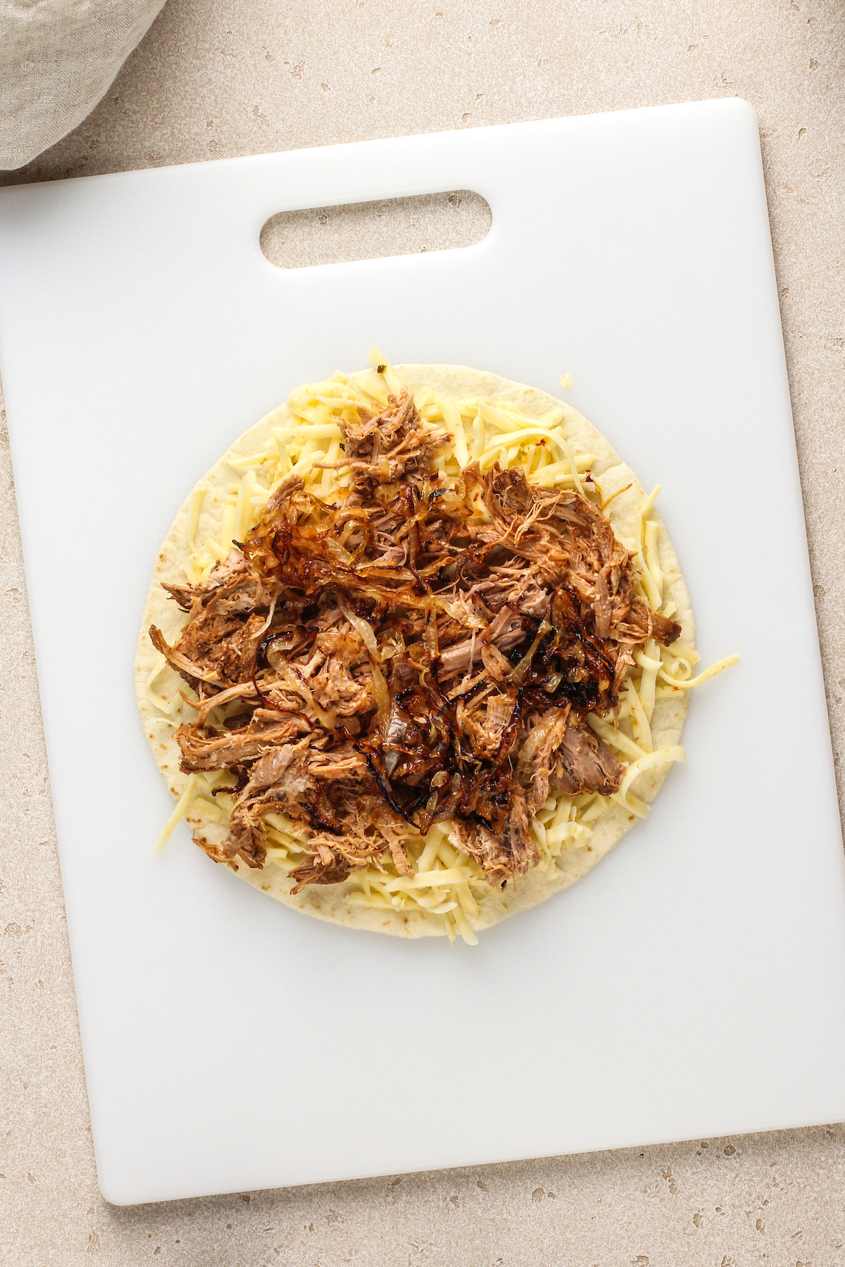 Assembling the quesadilla with pulled pork, cheese, and caramelized onions.