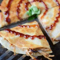 Sliced Pulled Pork and Caramelized Onion Quesadillas with barbecue sauce on top.