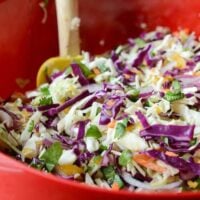 Spicy Mango Slaw in a red bowl with a wooden spoon.