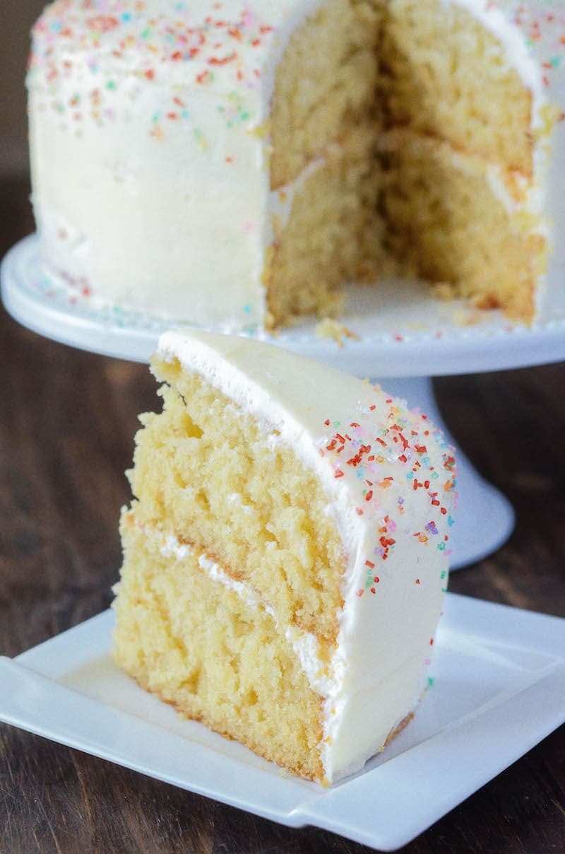 A cake on a pedestal with one slice cut out and set on a plate in front of it