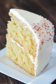 A slice of yellow cake on a plate with two layers separated by white frosting
