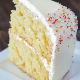 A slice of yellow cake on a plate with two layers separated by white frosting